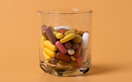 Стакан с разноцветными таблетками и капсулами на оранжевом фоне